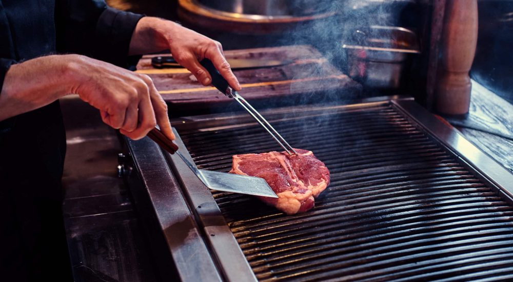 Master chef wearing uniform cooking delicious beef steak on a kitchen in a restaurant